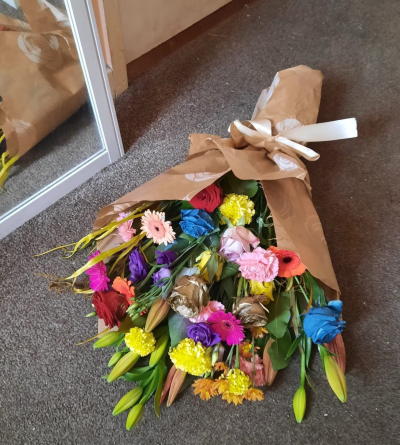 Rainbow Bloom Wrap - A bold and cheerful bouquet bursting with colour. Featuring bright gerberas, dyed roses, lilies, lisianthus, carnations and mixed seasonal blooms, this hand-tied wrap brings instant joy. Beautifully presented in kraft paper with a ribbon bow, perfect for birthdays, celebrations or anyone who loves vibrant flowers.