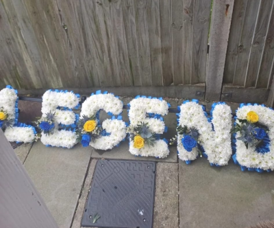 Personalised Letter Tribute - Various colour options with a matching ribbon. A bespoke funeral letter tribute, carefully handcrafted using fresh white blooms and accent flowers in your chosen colours. Created to spell a name or word, this meaningful arrangement offers a deeply personal way to honour and remember a loved one.