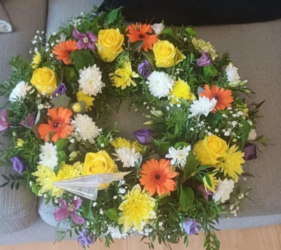 yellow orange purple funeral wreath - Vibrant celebration of life funeral wreath- cheerful circular tribute with yellow roses orange gerberas lisianthus, yellow spray chrysanthemums gypsophila and mixed seasonal foliag